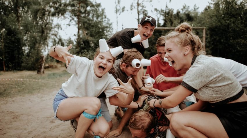 Energetic group of teenagers playing outdoors, with laughter and cups in a pile.